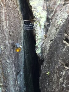 Narrow rock passage at Lookout Mountain marked by a sign reading “Fat Man Squeeze,” framed by steep, rugged stone walls with a caution light nearby—challenging even the boldest visitors.